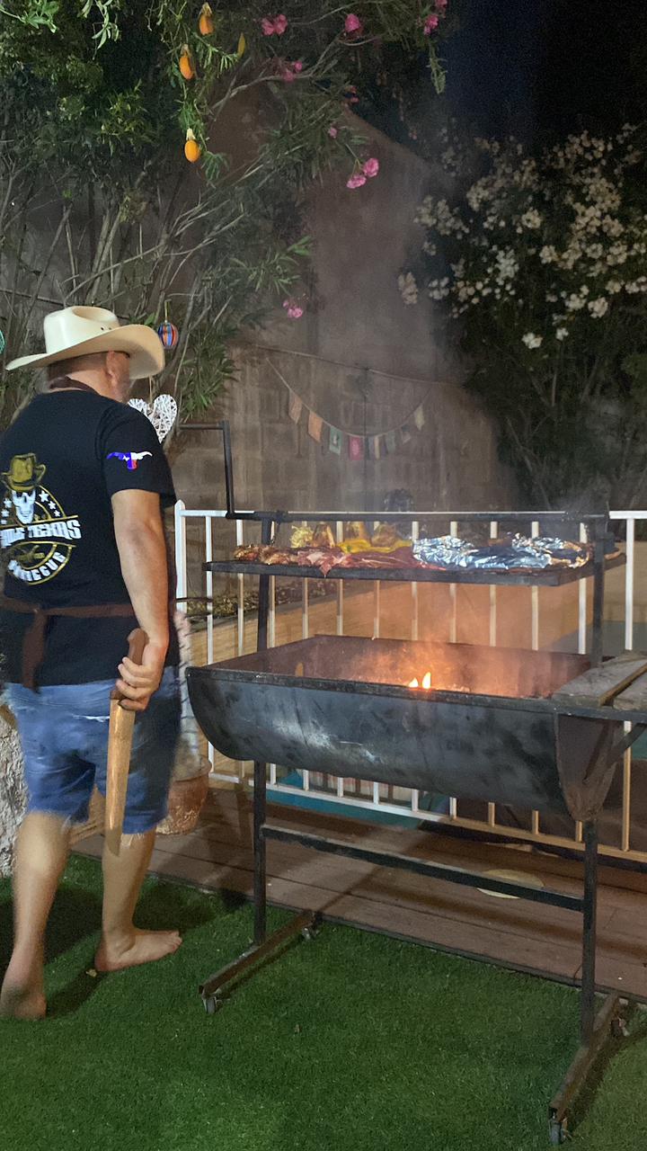 Pitmaster con sombrero junto al asador encendido durante un evento nocturno