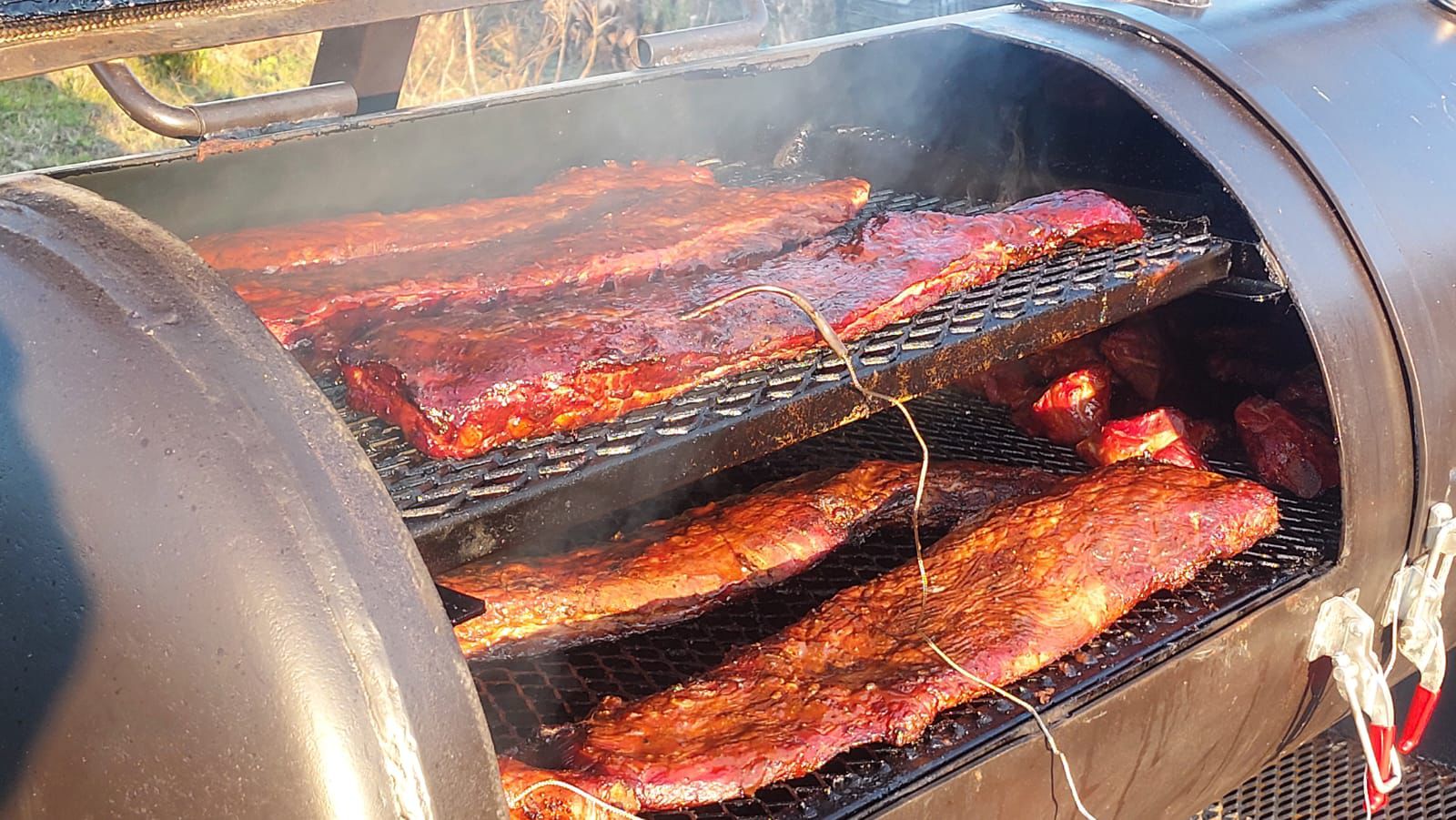 Costillar de cerdo ahumado a la leña sobre parrilla de ahumador, con humo elevándose